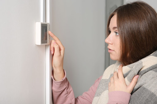 A woman adjusting a thermostat because the furnace is blowing cold air in a Greenville, SC home.